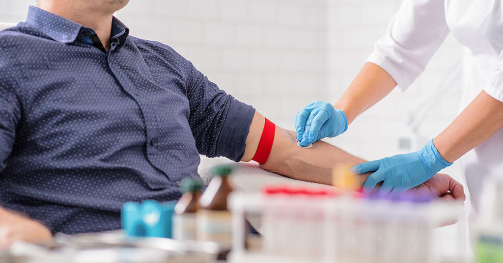 Hombre escuchando los beneficios de donar sangre mientras la especialista desinfecta el brazo previo al proceso de donación.