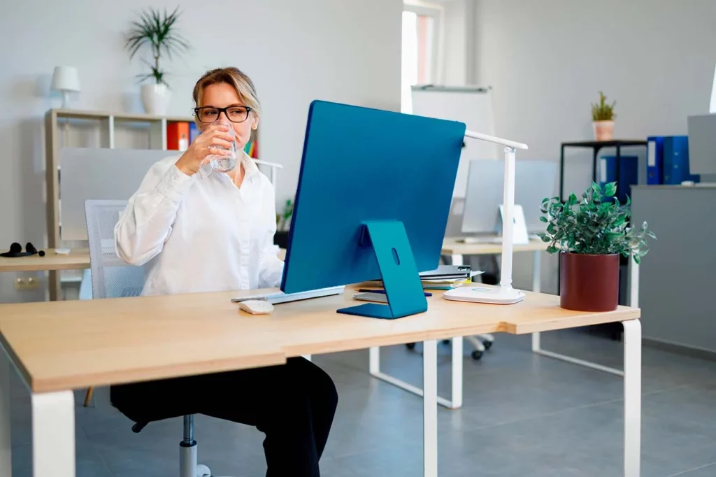 Mujer con lentes en oficina hidratándose en su trabajo 